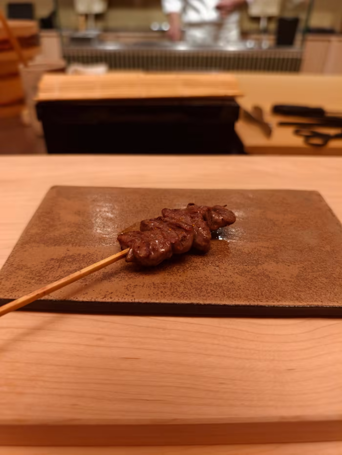 Yakitori skewer grilled over charcoal, served on a ceramic plate at the counter